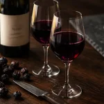 Vin syrah rouge, verres tulipe et raisins noirs sur table